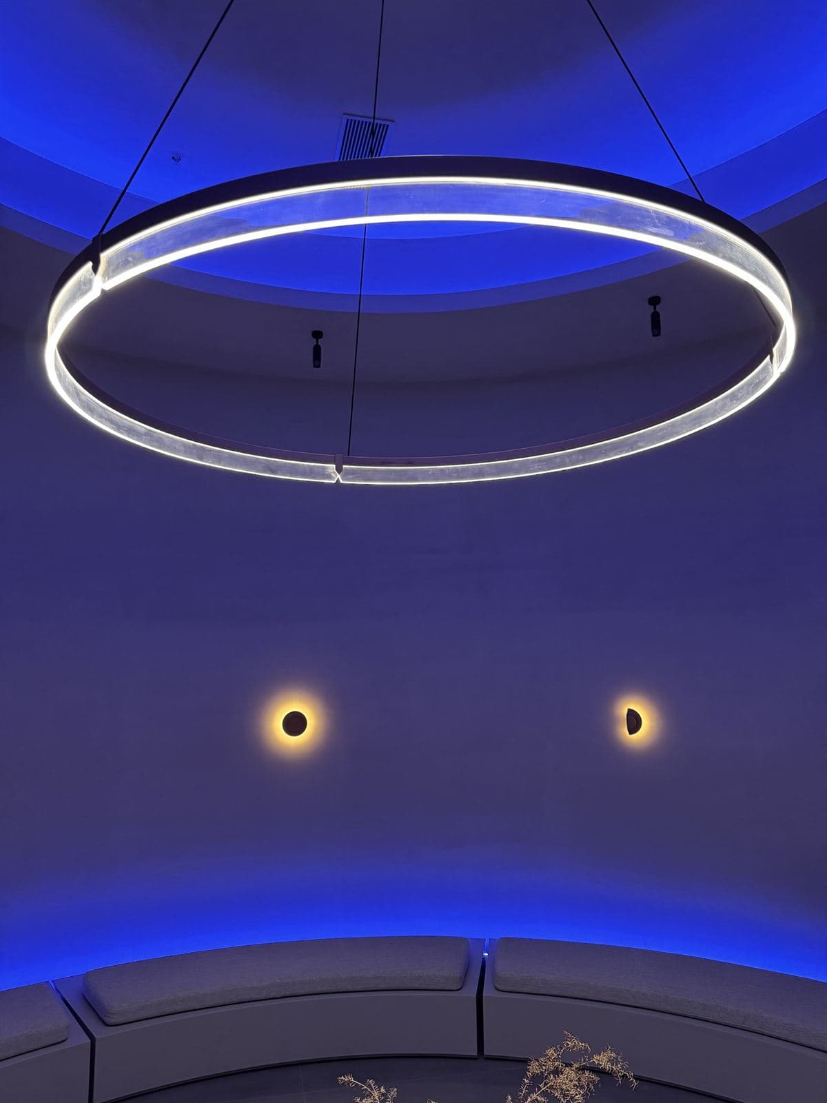 A large circular GUOCIO Halo pendant illuminates a room with blue accent lighting and two small wall sconces