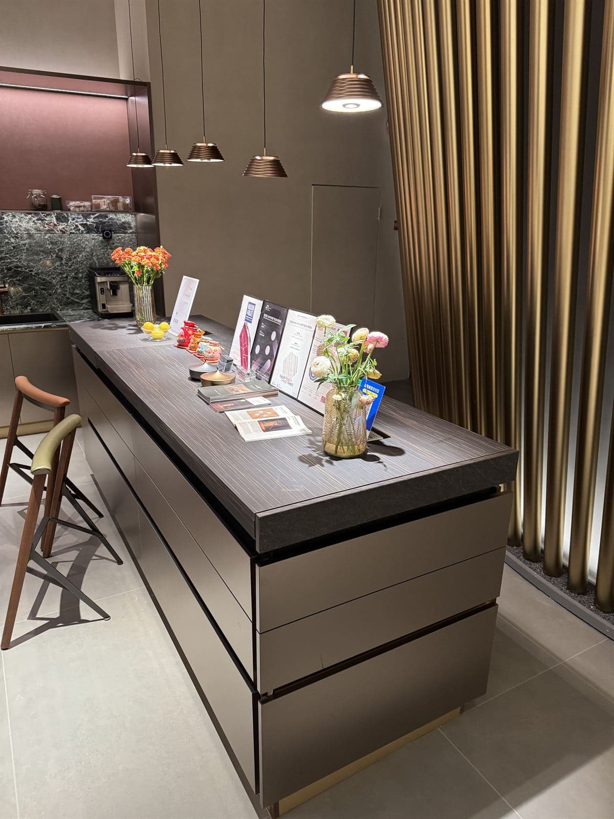 A modern kitchen island in dark wood and stone, lit by a cluster of small ribbed bronze GUOCIO pendant lights and one larger pendant