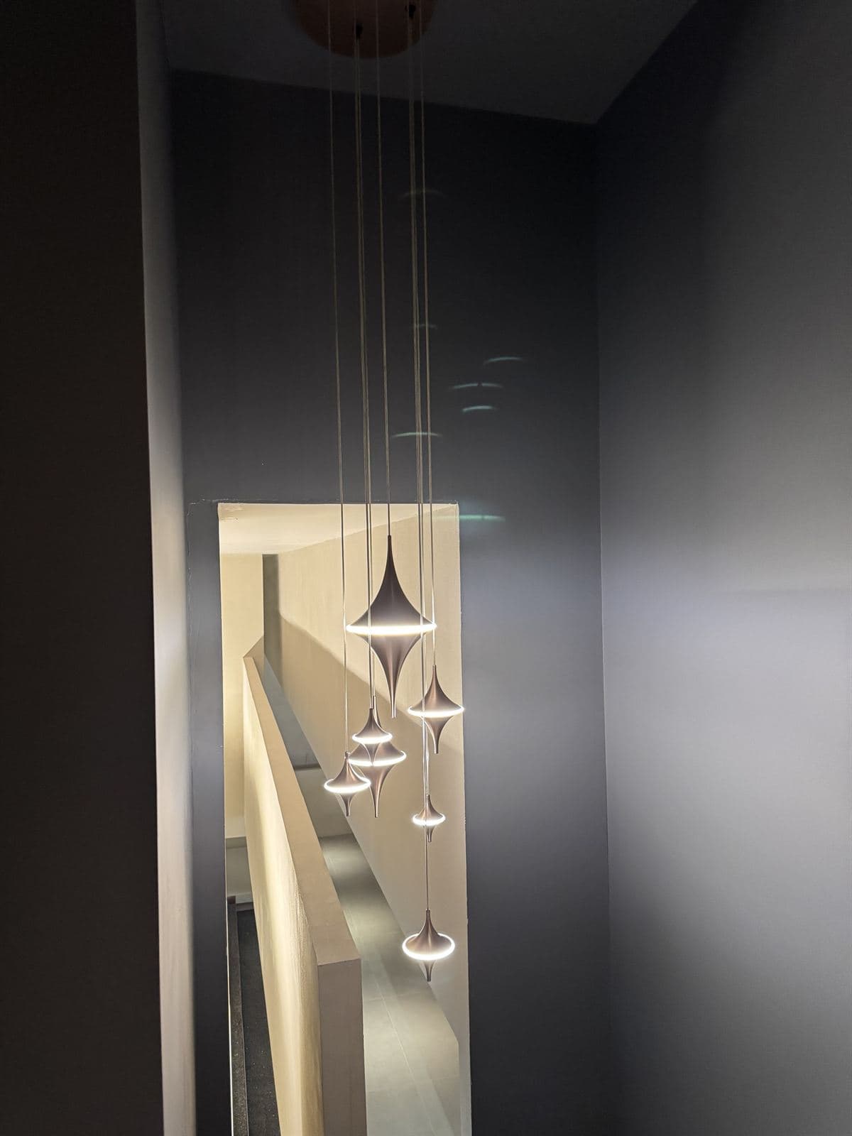 A series of modern GUOCIO pendant lights with a spinning-top design illuminating a dark stairwell