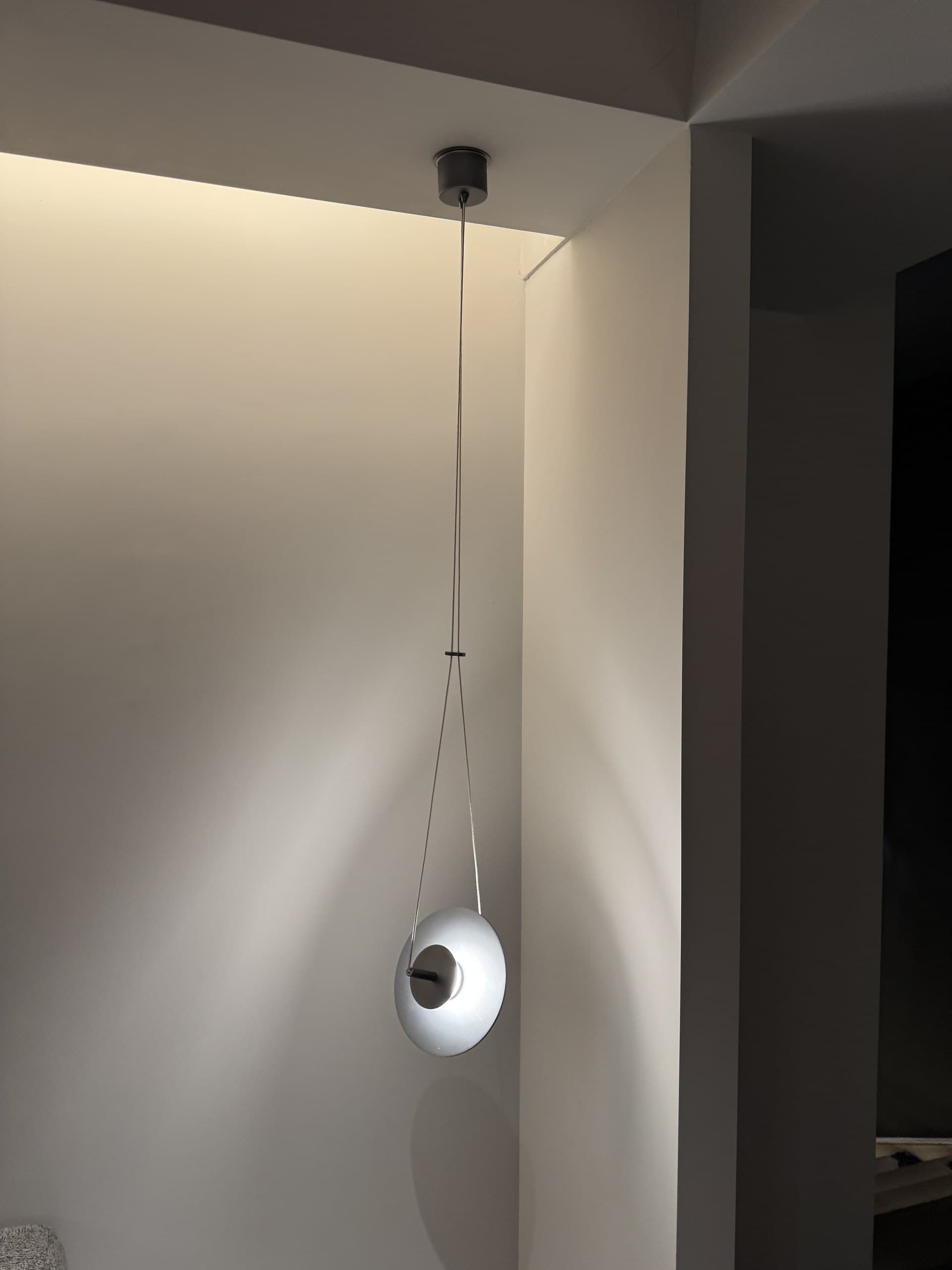 A modern pendant light with a circular shade hangs from the ceiling in a room with light-colored walls.