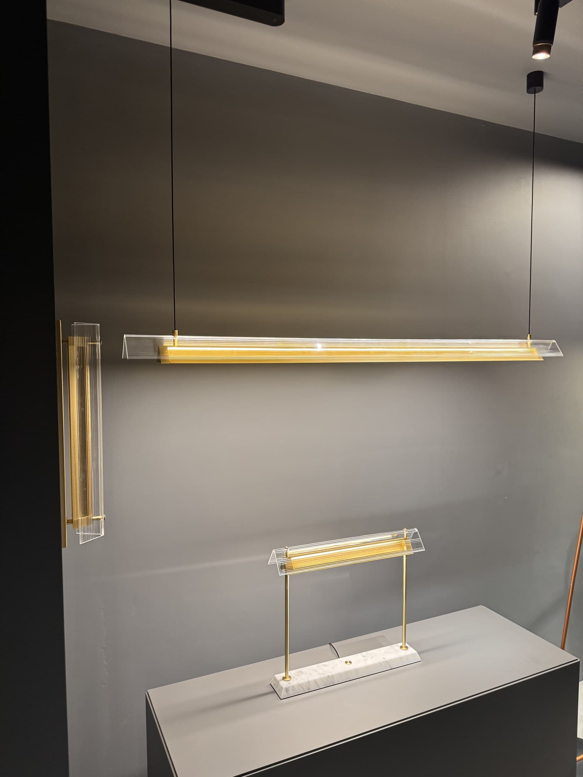 A collection of modern linear light fixtures with clear acrylic and gold accents displayed against a dark gray wall.
