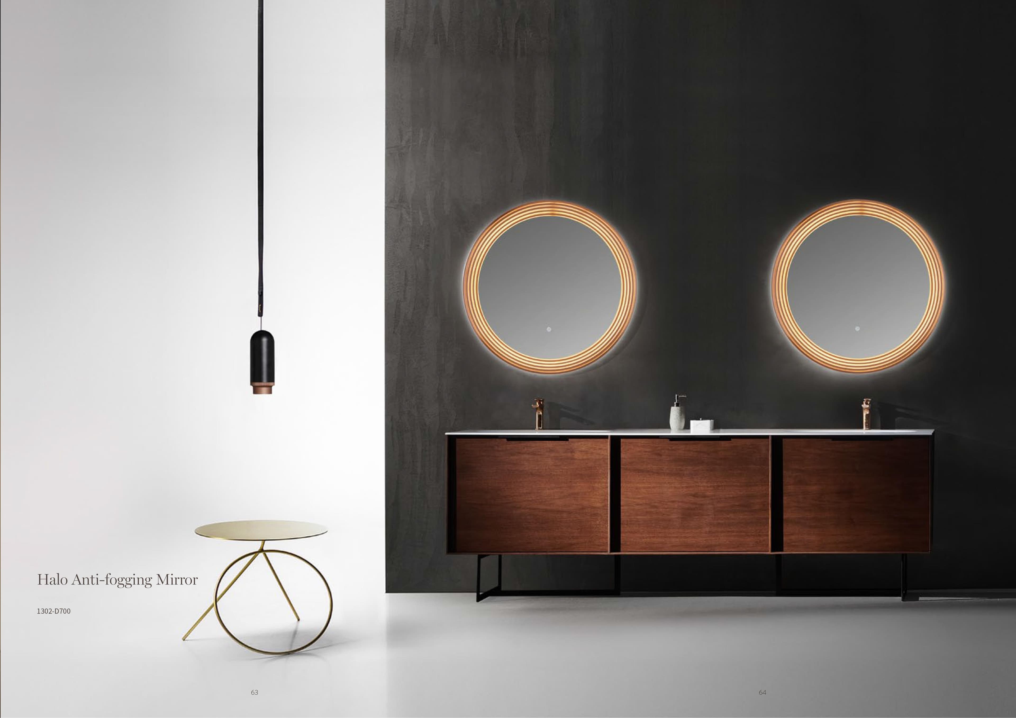 A modern bathroom features a dark gray wall with two round, backlit mirrors above a wooden double vanity with white countertops, and a minimalist pendant light hangs on the left against a white wall.