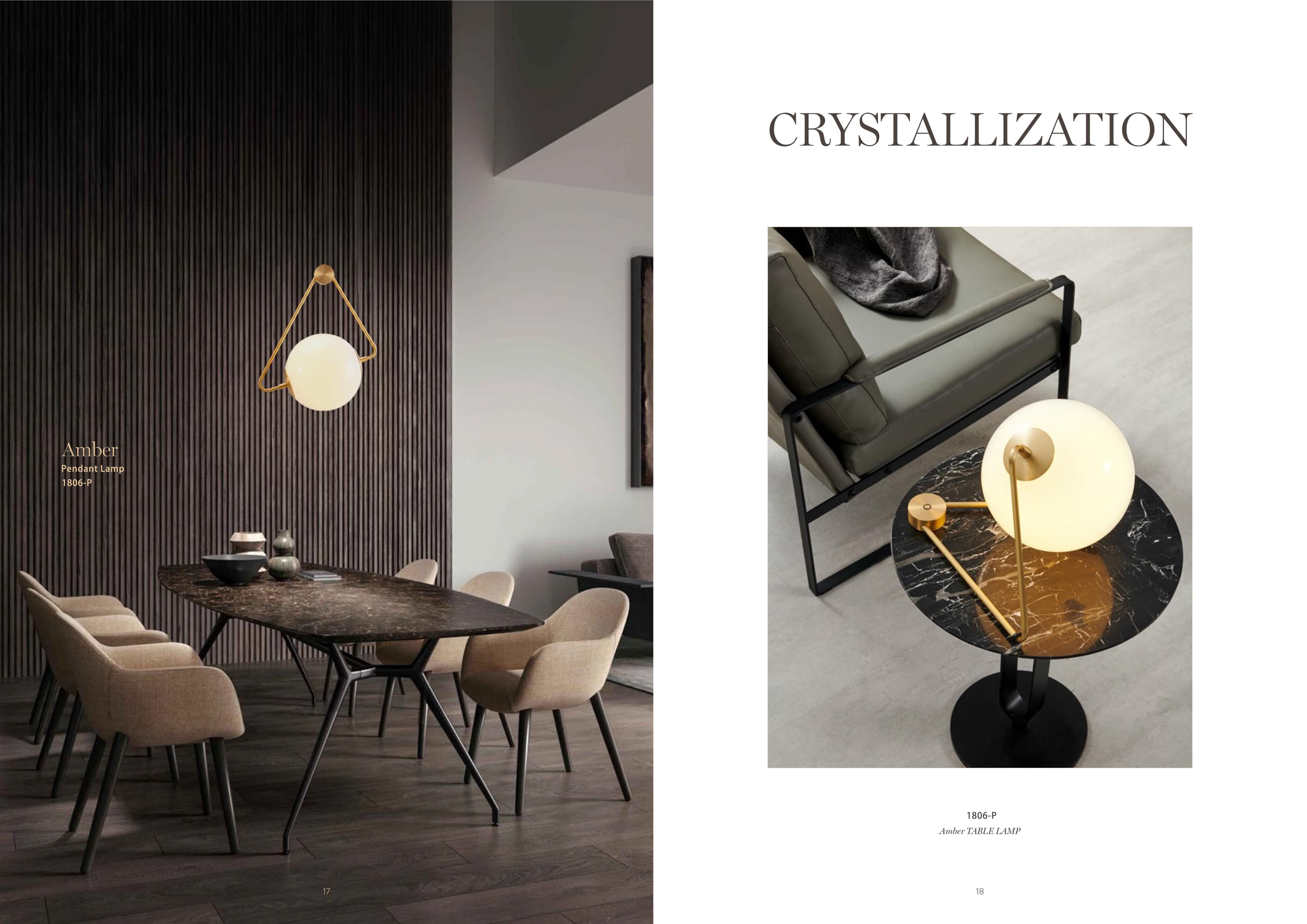 A modern dining room features a long dark marble table surrounded by beige upholstered chairs, illuminated by a unique pendant lamp with a spherical white shade and a golden triangular frame, while a matching table lamp sits on a round marble side table next to a grey armchair.